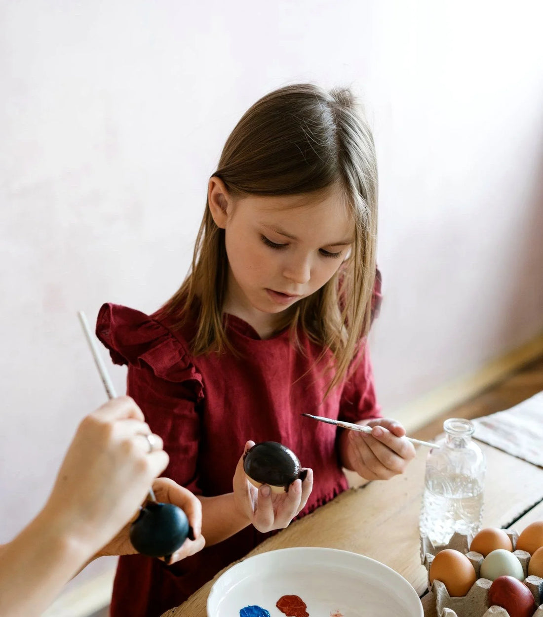 Smiling girl painting a white Plaster of Paris figure with a blue brush at a craft table