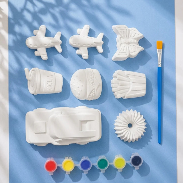Planes and fast food Plaster of Paris mix kit — 8 white figures with 6-colour paint strip and brush on light blue background